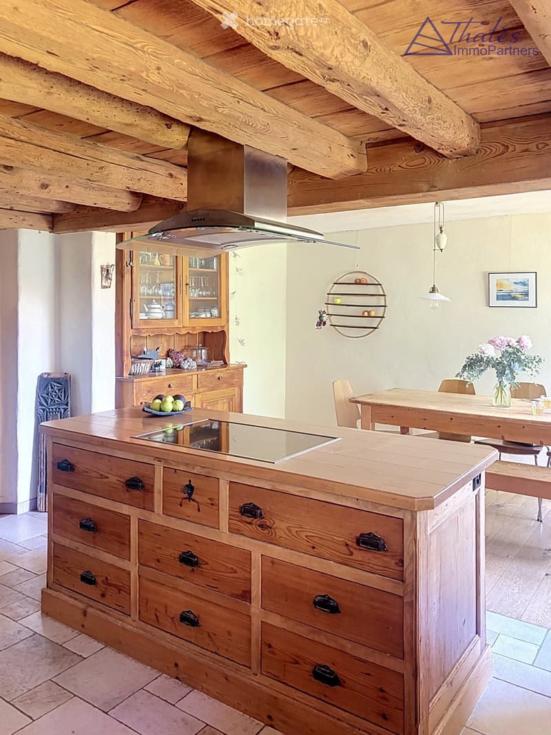 A rustic kitchen with a wooden island, cabinets, a dining table, and hanging pendant lights.