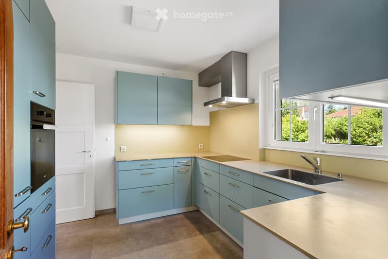 Modern kitchen with light blue cabinets, a central island, and stainless steel appliances including a sink, faucet, and oven.