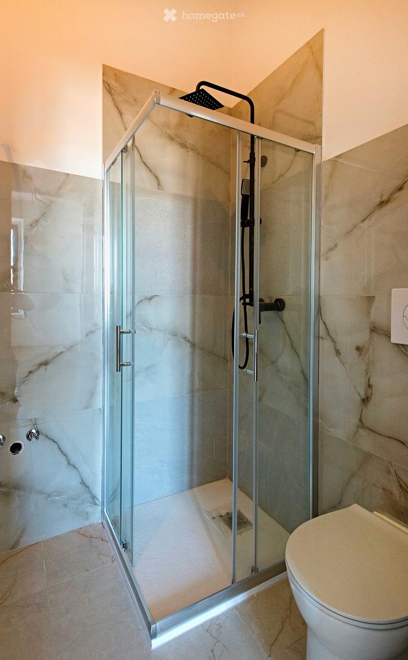 Modern bathroom with marble tiles, glass-enclosed shower, and a toilet. Features a sleek showerhead and modern fixtures.
