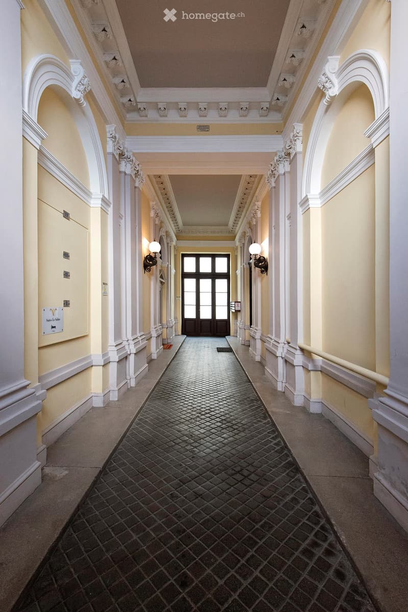 Elegant hallway with a patterned tile floor, white columns, arched doorways, and decorative wall sconces.