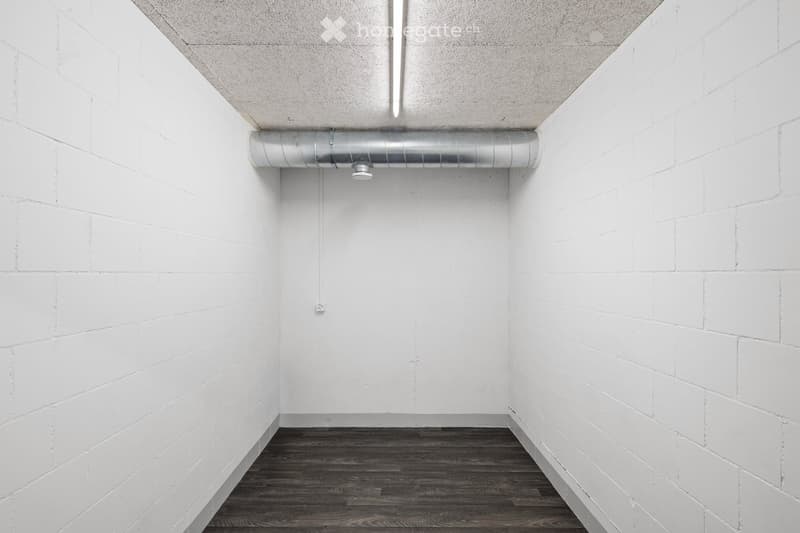 Completely empty room with white brick walls, dark wooden floor, and exposed metal ductwork on the ceiling.