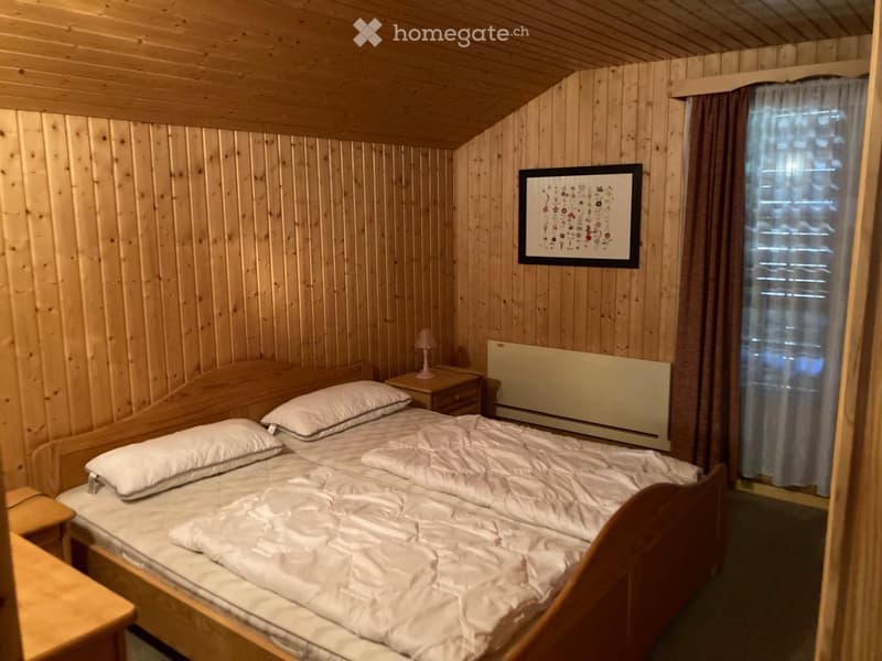 Cozy wooden bedroom with a double bed, nightstand, lamp, and a framed picture on the wall.