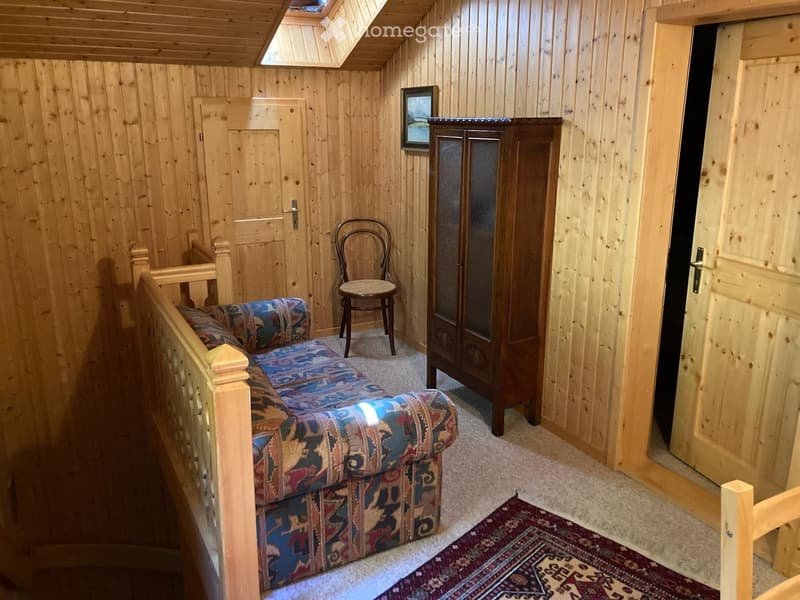 Cozy wooden-paneled room with a patterned sofa, wooden chair, cabinet, and a small picture frame on the wall.