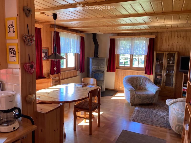 Cozy living room with wooden beams, fireplace, sofa, armchair, dining table, and coffee maker.