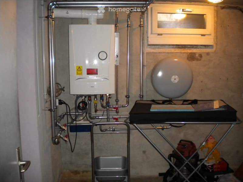 Utility room with a water heater, water tank, table, stool, and trash bin.