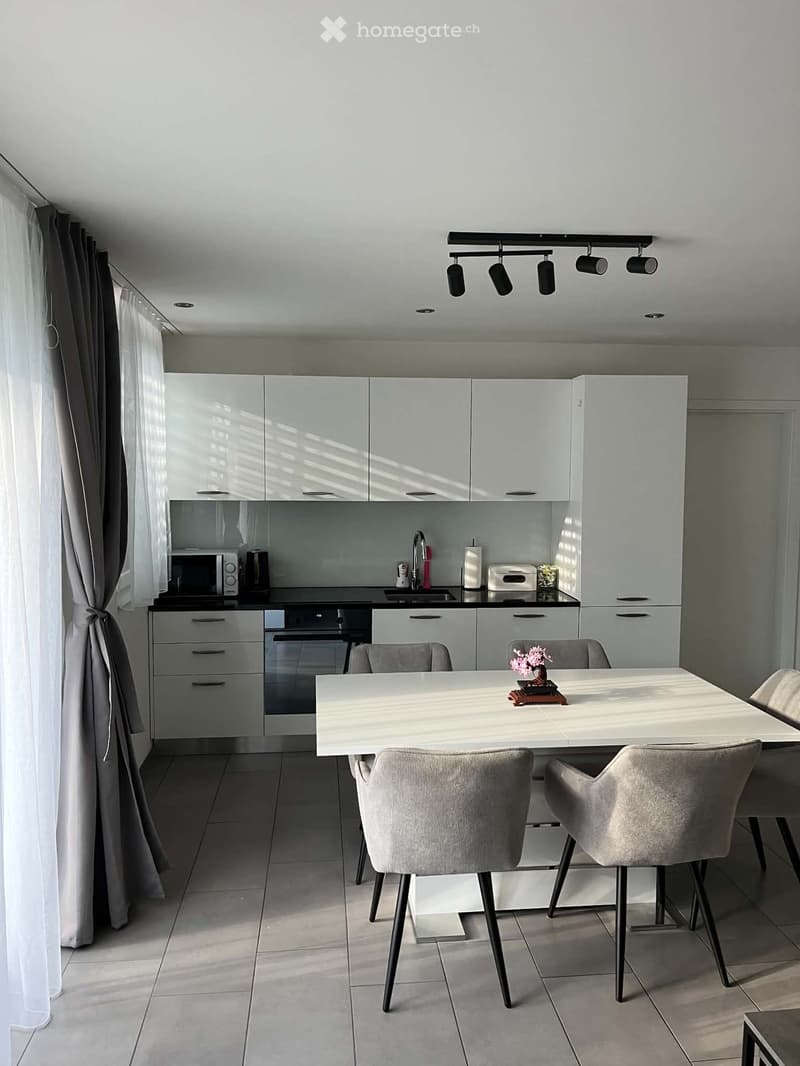 Modern kitchen with white cabinetry, stainless steel appliances, a central island, and a dining area with a white table and four grey chairs.