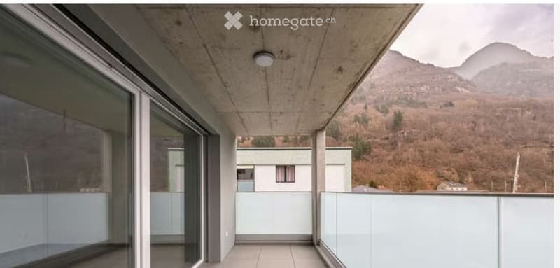 Modern balcony with large glass panels, concrete ceiling, and scenic mountain view.