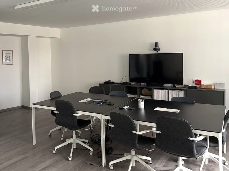 Modern conference room with a large black table, multiple chairs, a large screen mounted on the wall, and a cabinet with books and office supplies.