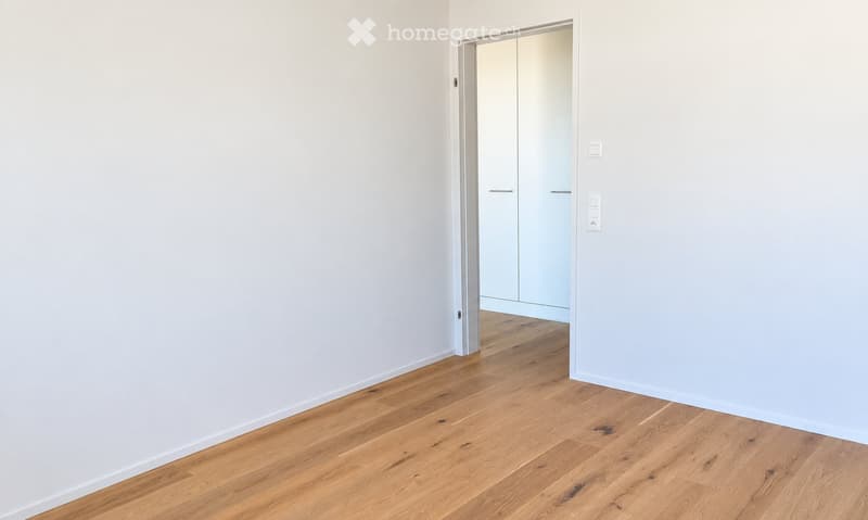 Empty room with light-colored walls and wooden flooring, featuring a doorway leading to another room with built-in wardrobes.