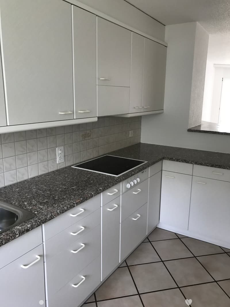 Modern kitchen with white cabinets, granite countertops, and an induction stove. The space features tiled walls and a tiled floor.