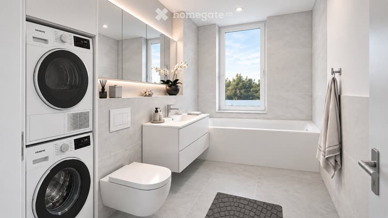 Modern bathroom with a white washing machine and dryer, toilet, sink, bathtub, large mirror, and a window with a view of greenery.