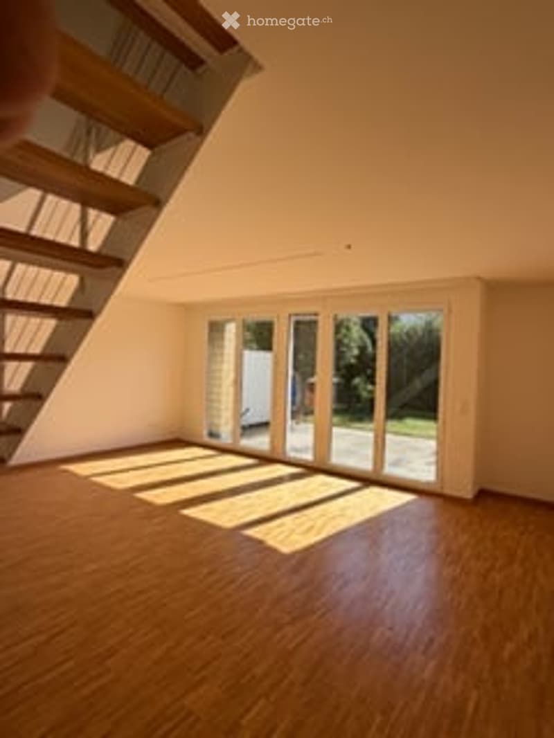 Bright, empty room with wooden flooring, large glass sliding doors leading to a balcony, and natural light streaming in.