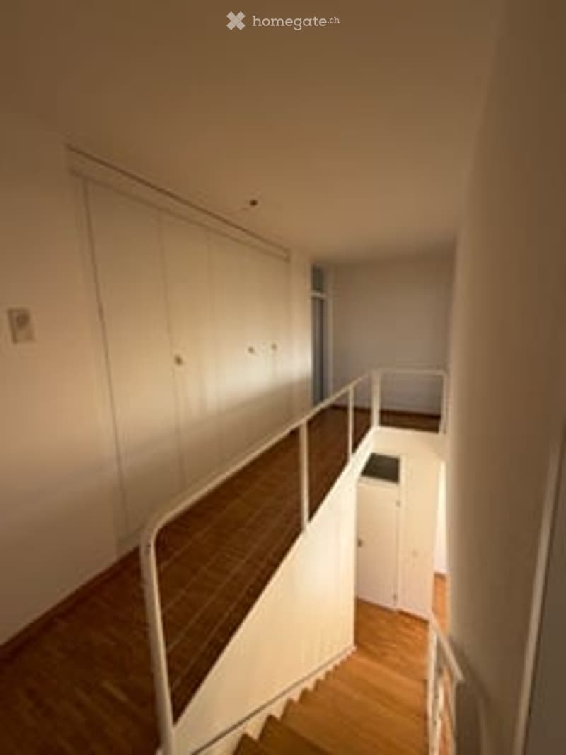 Empty staircase leading to an upper level, with wooden steps and a white railing, adjacent to a small white closet area.
