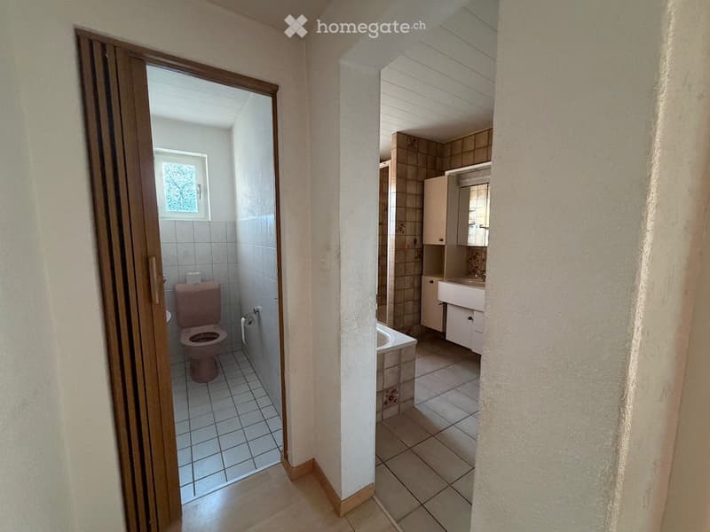 Two adjacent bathrooms with tiled floors and walls, one with a toilet and the other with a sink, bathtub, and cabinet.