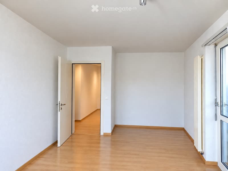 Empty hallway with light wooden flooring, white walls, and a partially open door leading to another room.