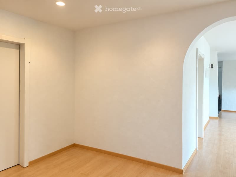 Empty hallway with light-colored walls, wooden flooring, and a single door on the left side.