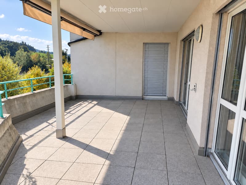 Balcony with tiled floor, white walls, large windows, and a scenic view of greenery and hills.