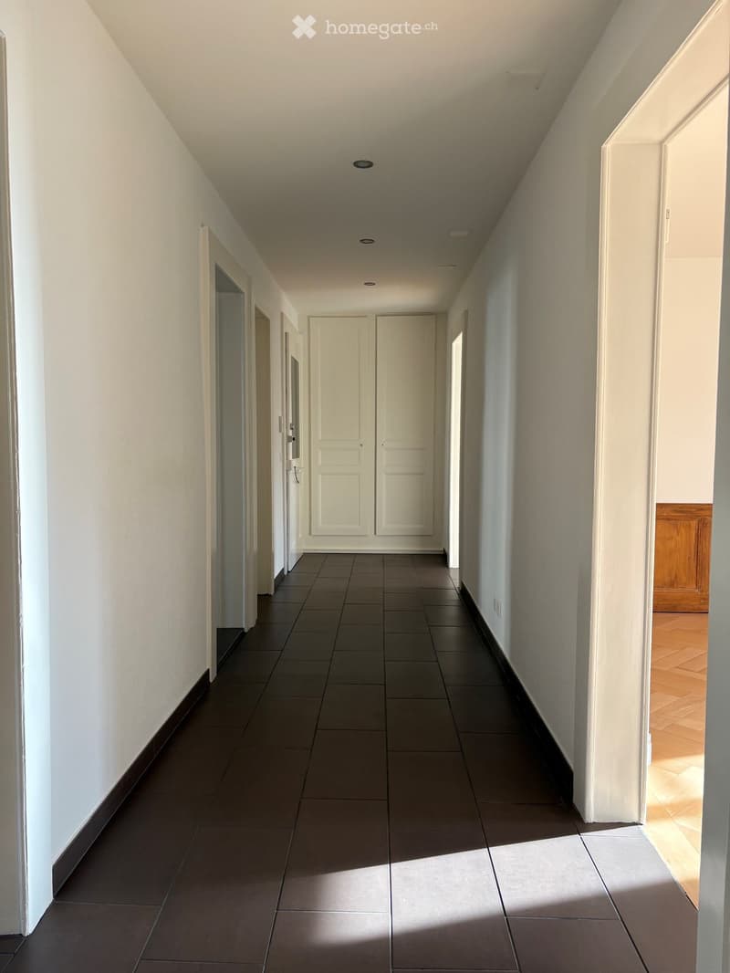 Empty hallway with tiled floor, white walls, and several doors leading to rooms.