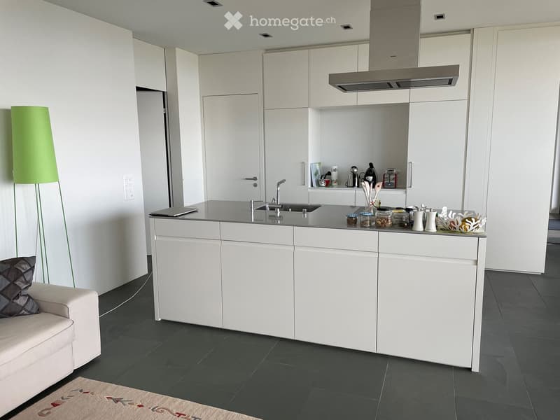 Modern kitchen with white cabinets, island, and stainless steel appliances. Includes a sofa, floor lamp, and various kitchen items on the island.