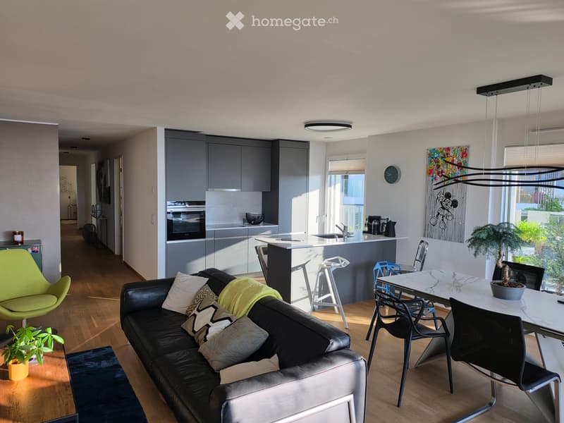 Modern living and dining area with a black leather sofa, green armchair, coffee table, dining table with chairs, kitchen island, and various decorative items.