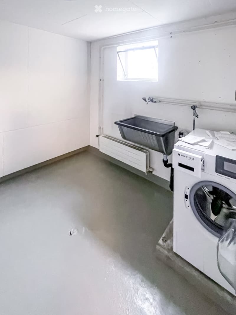 Empty room with a washing machine, sink, and radiator. Bare walls and floor, no furniture.
