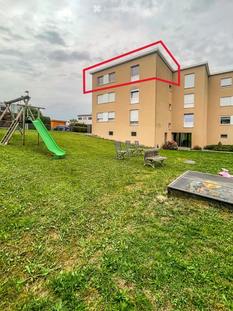 A grassy outdoor area with a playground featuring a green slide and climbing frame, several outdoor chairs and tables, and a raised garden bed with toys inside.