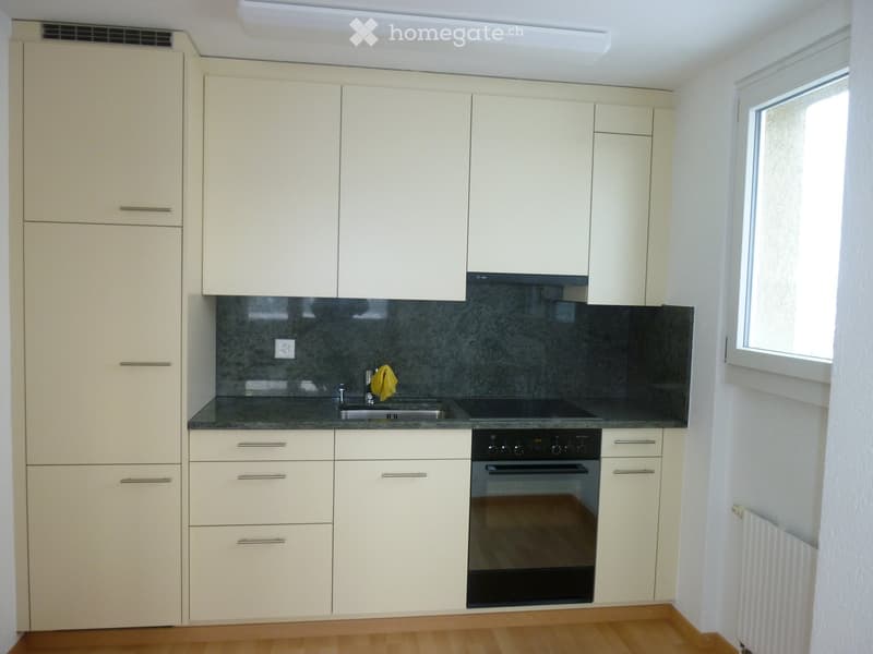 Modern kitchen with white cabinets, dark countertop, sink, and built-in oven. Features a window on the right side.