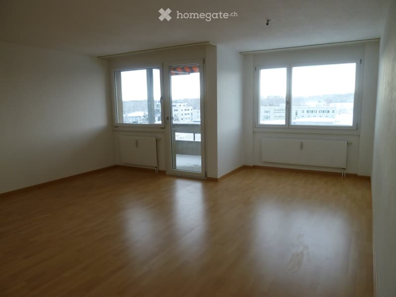 Empty room with wooden flooring, white walls, large windows, and a sliding glass door leading to a balcony.