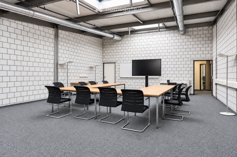 Modern meeting room with grey carpet, white tiled walls, large screen, tables, and black chairs.