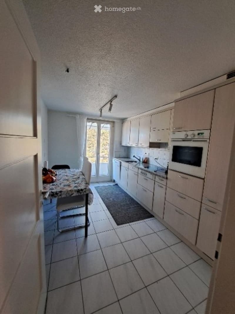 Modern kitchen with white cabinets, tiled floor, and a small dining area with a table and chairs.