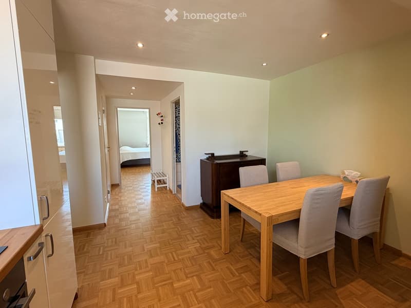 Dining area with a wooden dining table and four chairs, a dark wooden cabinet, and a hallway leading to a bedroom.