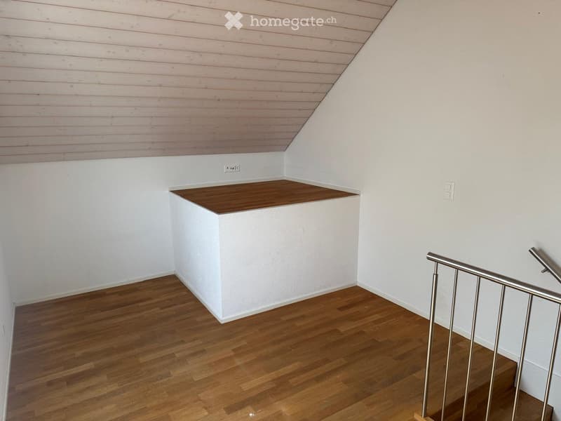 Empty hallway with wooden flooring, white walls, and a small built-in shelf. Metal railing visible on the right side.