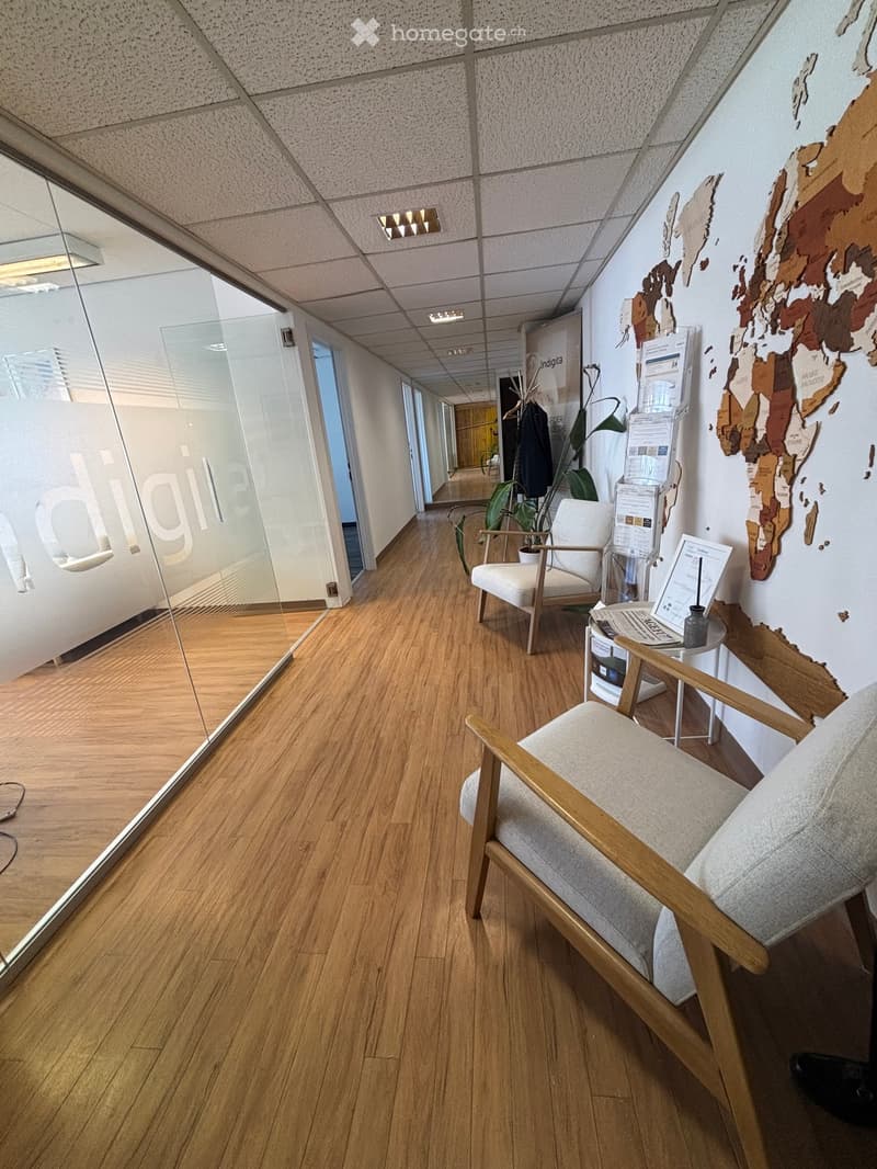 Modern hallway with wooden flooring, glass walls, and a seating area featuring a chair, small table, and plant.