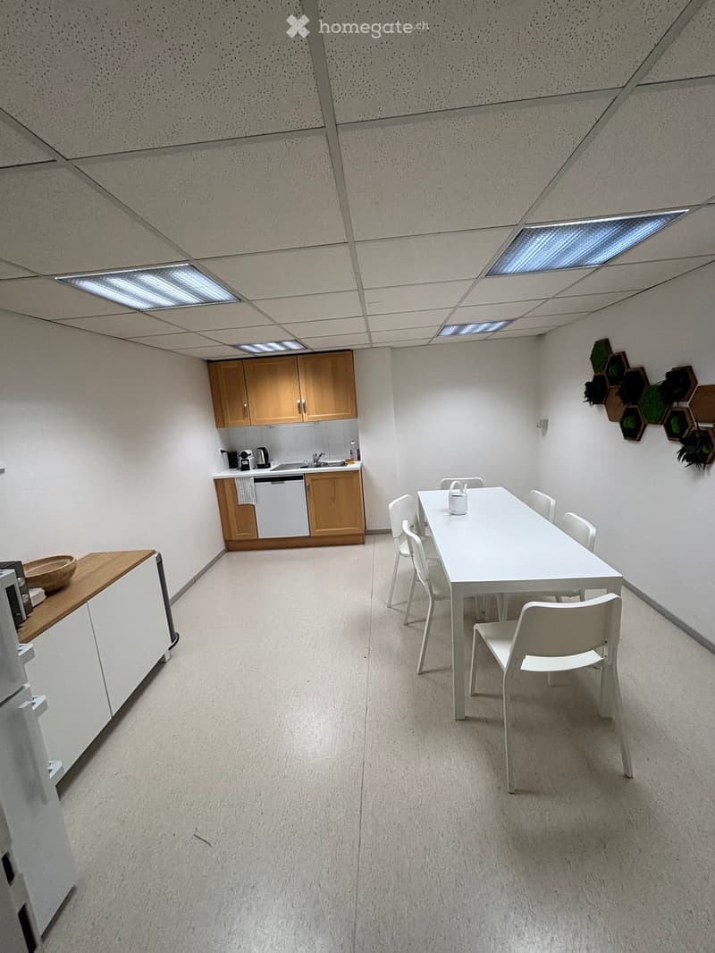 A modern, minimalist kitchen and dining area with white walls, light wood cabinets, a white dining table with chairs, and a small sink area.