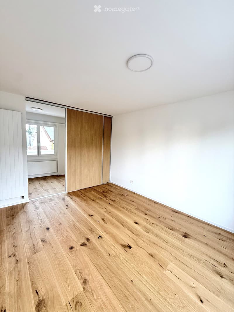 Empty room with light wooden flooring, white walls, and a large sliding closet door. A round ceiling light fixture is visible.