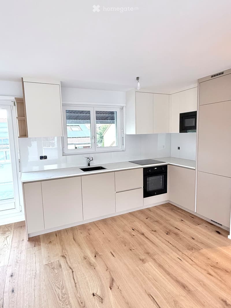Modern kitchen with light-colored cabinets, a sink, an oven, and a microwave, featuring wooden flooring and a large window.