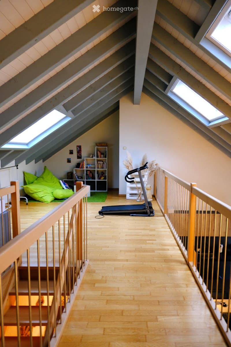 Loft-style room with wooden flooring, exposed wooden beams, skylights, a green bean bag chair, a bookshelf, and a treadmill.