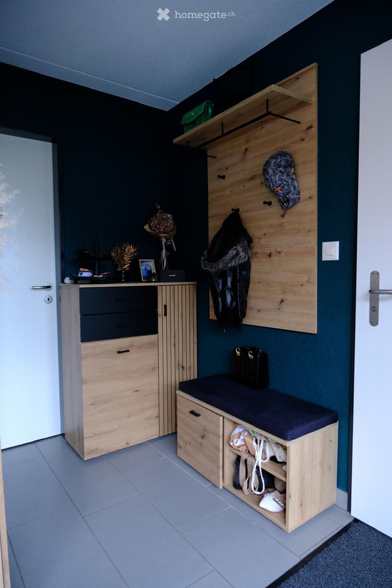 A modern, well-organized entryway with a wooden bench, storage cabinet, shelves, and decorative items.