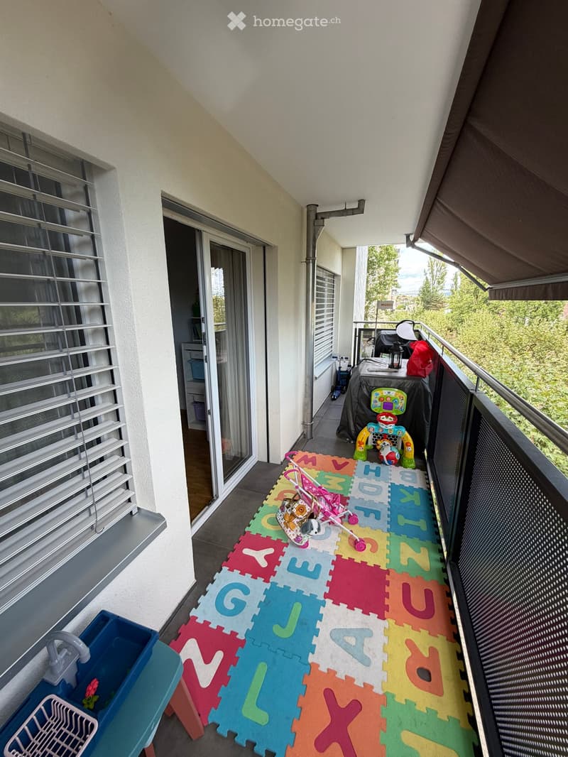 Balcony with colorful foam mat, stroller, toy, and outdoor furniture.