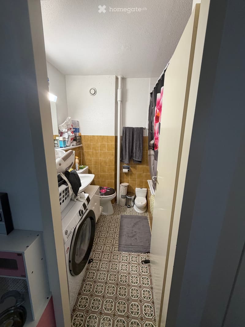 Small bathroom with a washing machine, toilet, sink, towels, and a shower curtain.