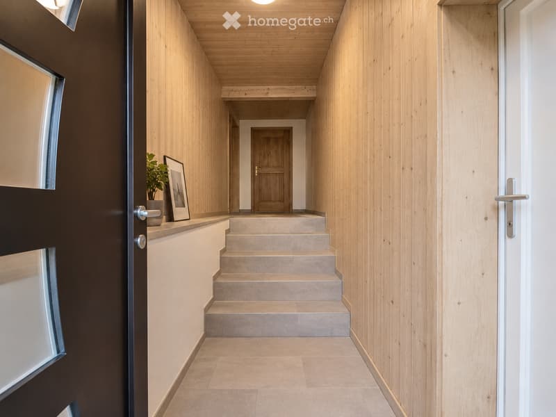 Modern hallway with wooden panel walls, a small staircase leading upwards, and a potted plant on a shelf.