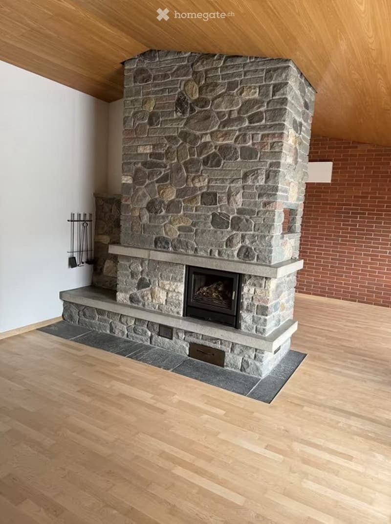 Modern living room with a stone fireplace, wooden flooring, and white walls.