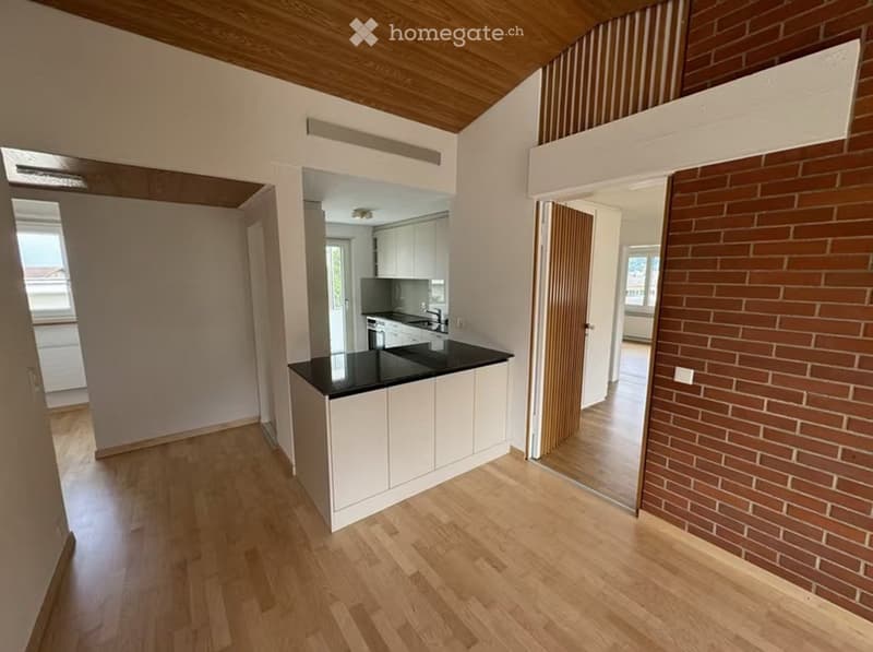 Open-plan kitchen area with white cabinets, black countertop, and a central island. Wooden flooring and exposed wooden ceiling beams.