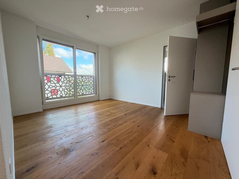Empty room with wooden flooring, white walls, and a large window with a view of a house and balcony.