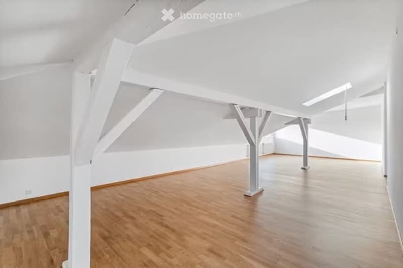Empty room with wooden flooring and white walls, featuring exposed white beams and a high ceiling.