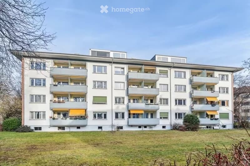 Multi-story residential building with multiple balconies and yellow awnings, surrounded by a grassy area.