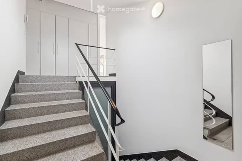 Modern hallway with a staircase featuring a sleek metal railing and grey steps, white walls, and built-in white cabinets.