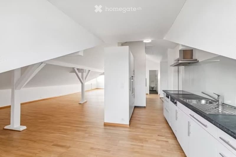 Bright, open kitchen and living area with white walls, wooden flooring, and modern kitchen cabinets.