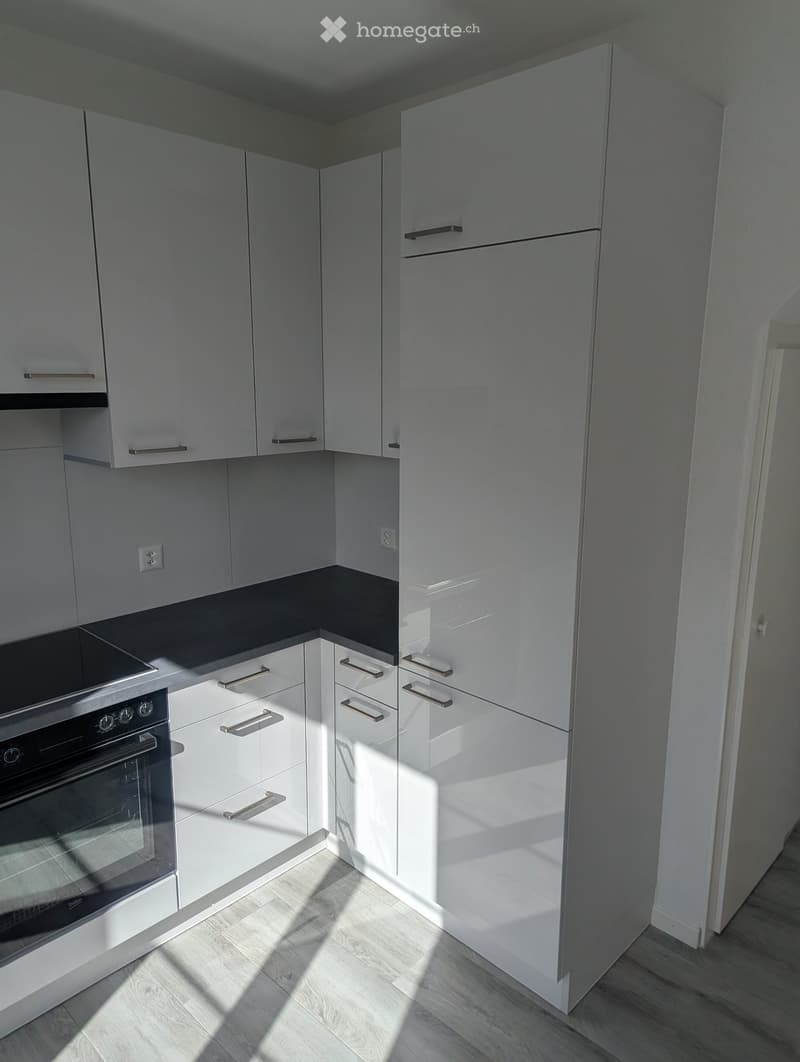 Modern kitchen with white cabinets, stainless steel oven, and light wooden flooring.