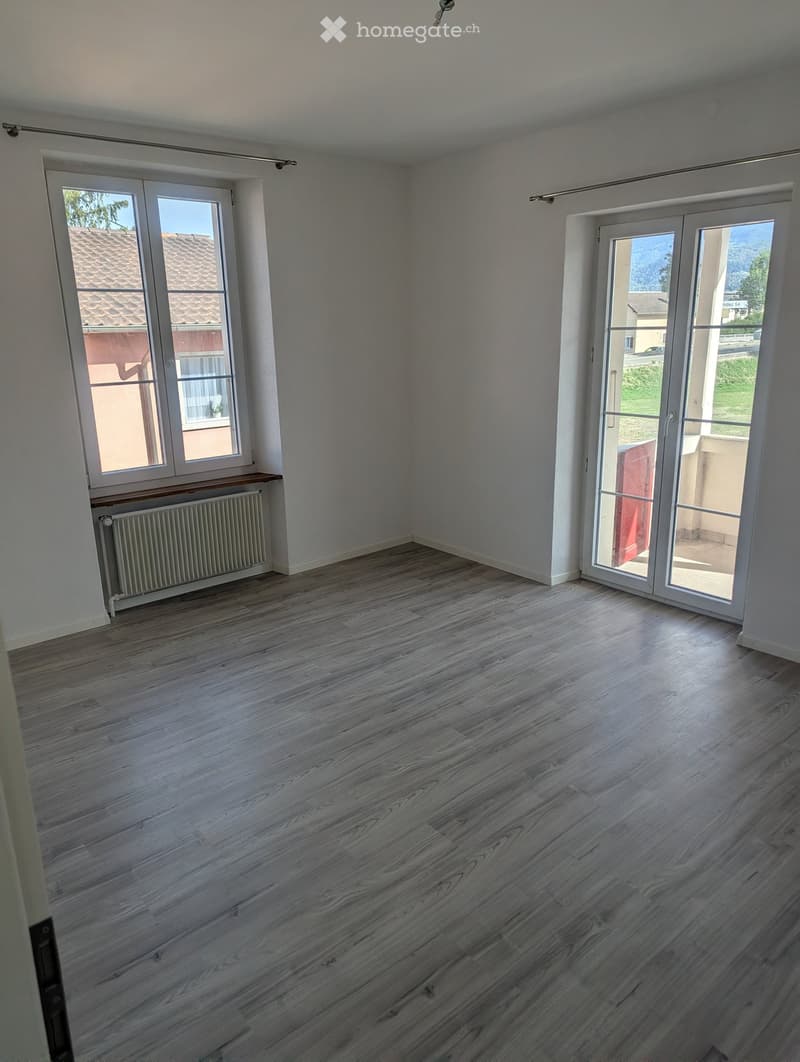 Empty room with wooden flooring, white walls, large windows, and a radiator. No furniture or equipment present.